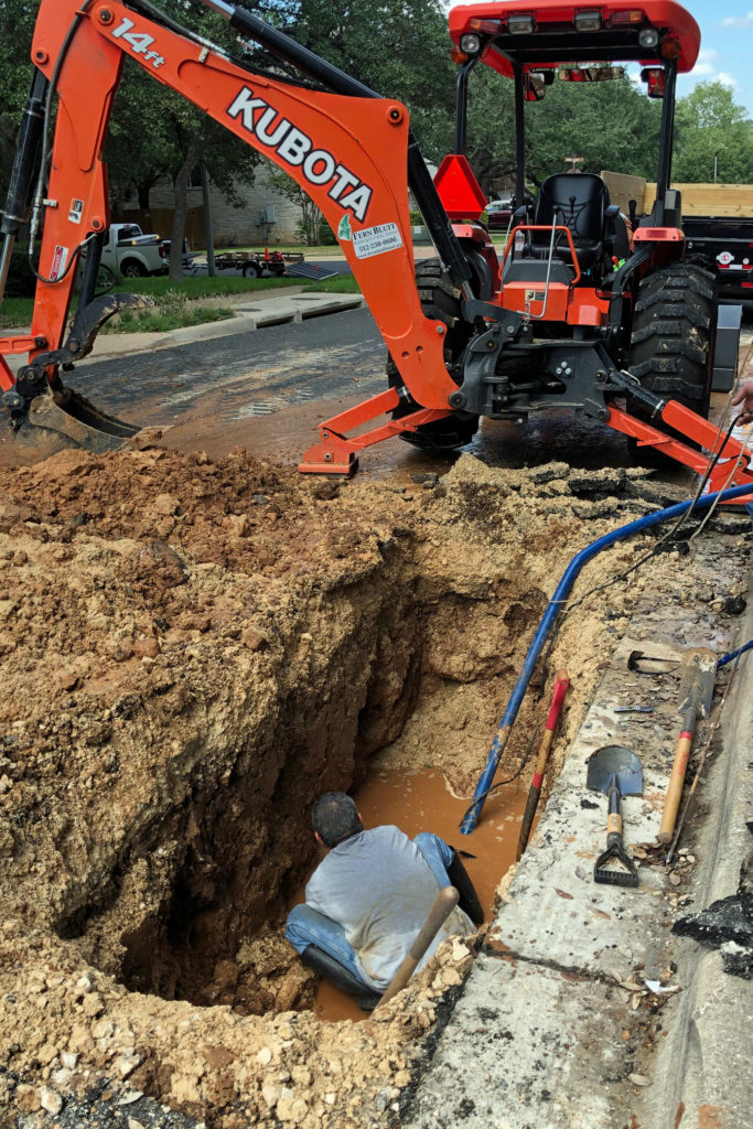 Picture of utility worker in large hole making repairs.